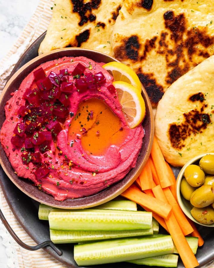 beet hummus in a bowl surrounded by flatbread and veg