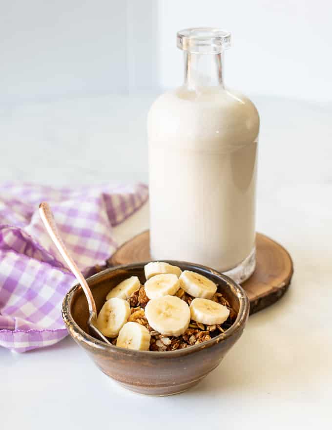 A bowl of granola with banana and a bottle of milk 