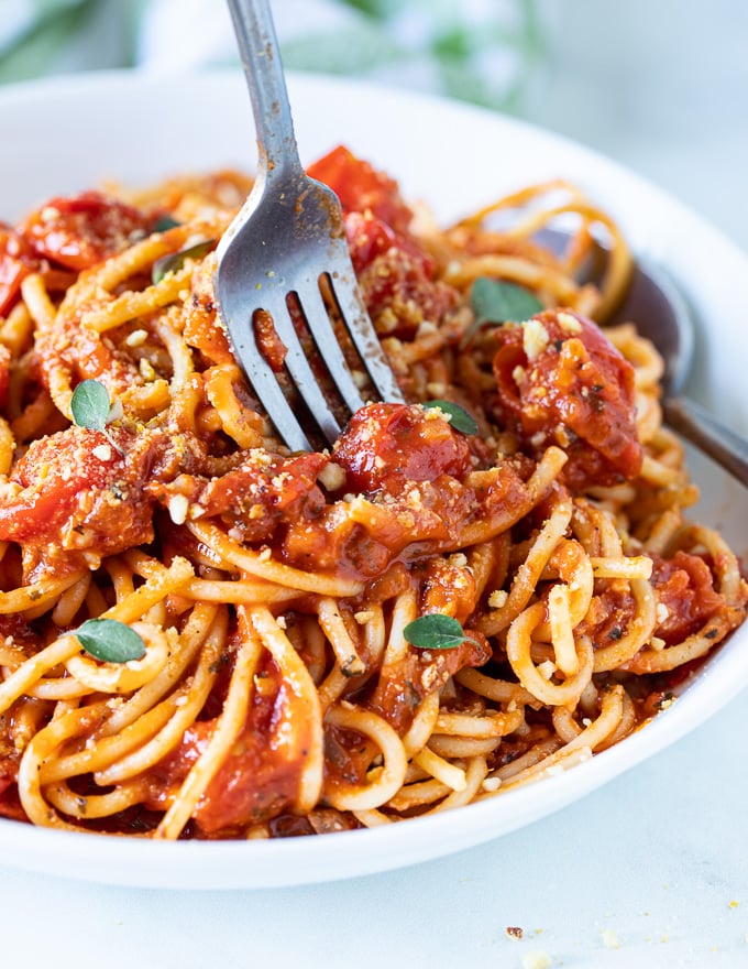 a fork about to dig into a bowl of spaghetti tossed in cherry tomato sauce