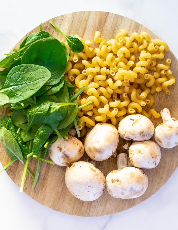 pasta spirals, mushrooms and spinach on a wooden board, ready to make creamy vegan mushroom pasta 