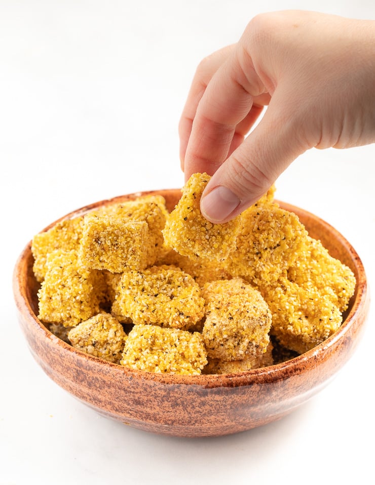 Crispy tofu in a bowl with a hand taking a piece