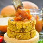 two curried chickpea burgers stacked on a bun with a generous spoon of mango chutney being dolloped on top