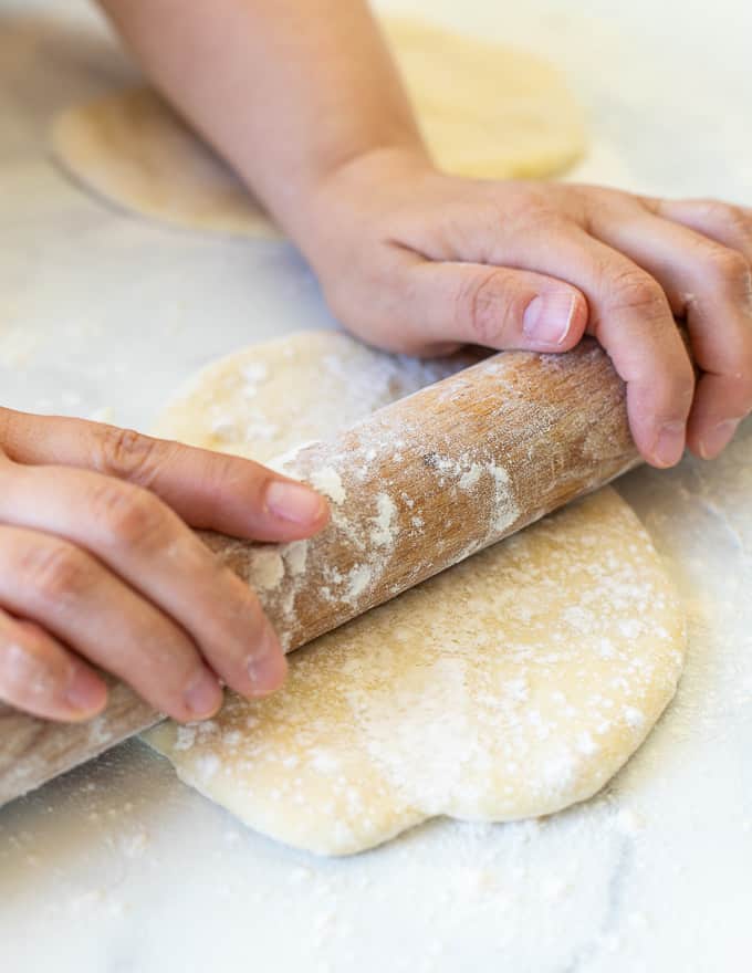 flatbread dough being rolled out with a rolling pin