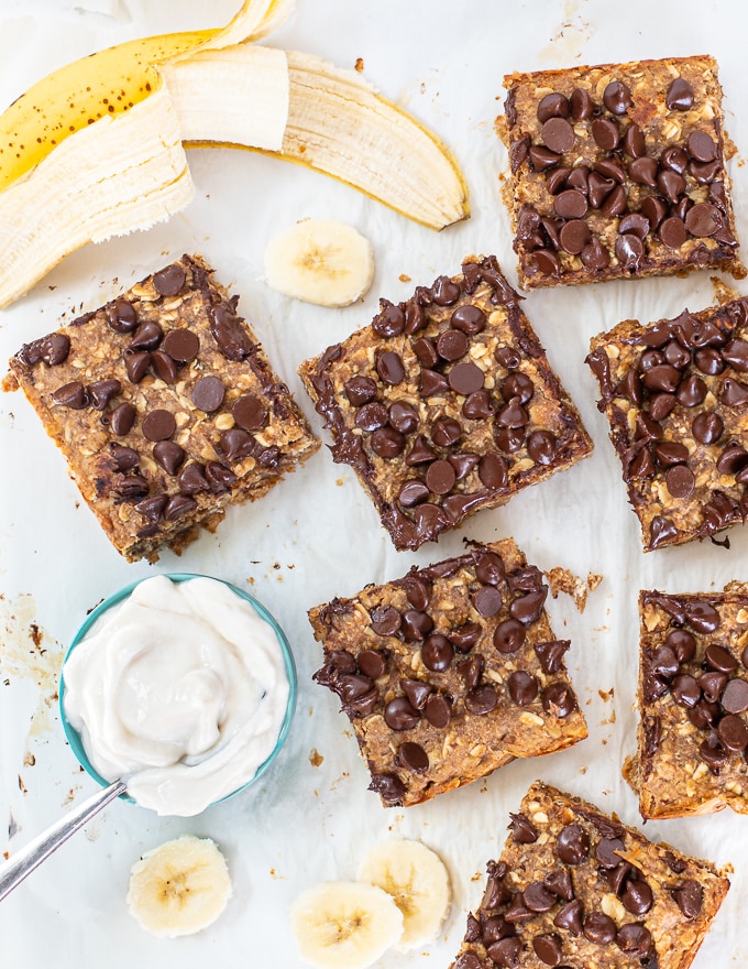 healthy breakfast bars sliced up on a white background with a bowl of yogurt and a banana cut into slices 