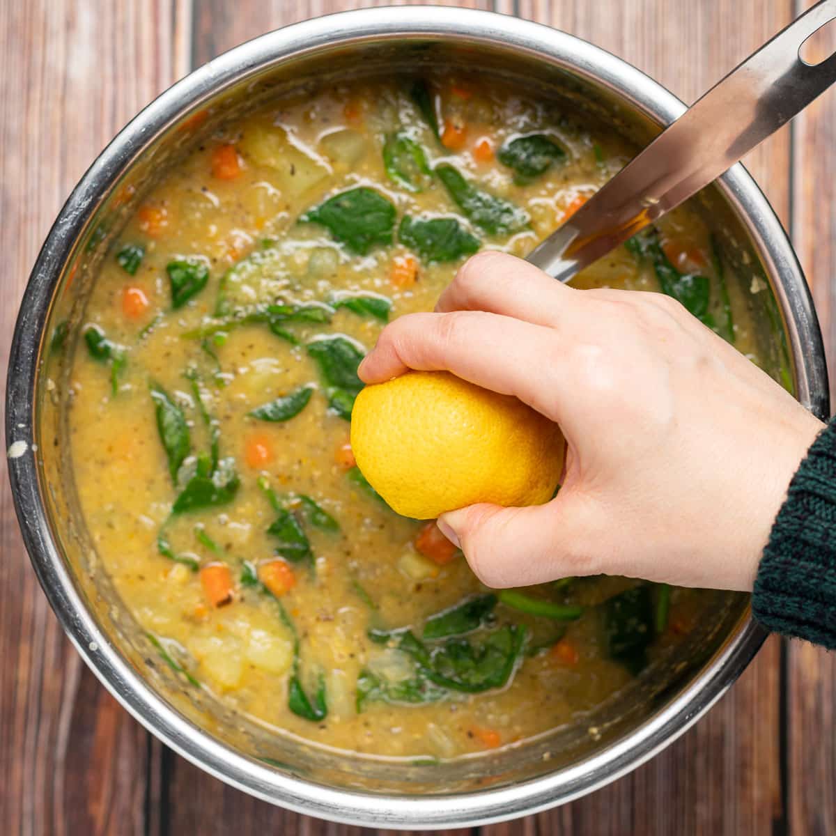 lemon being squeezed into a pot of soup