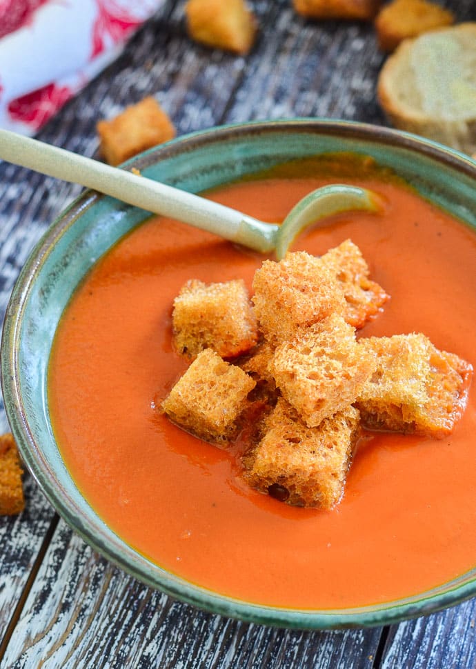 A bowl of tomato soup with croutons and a cute green ceramic spoon