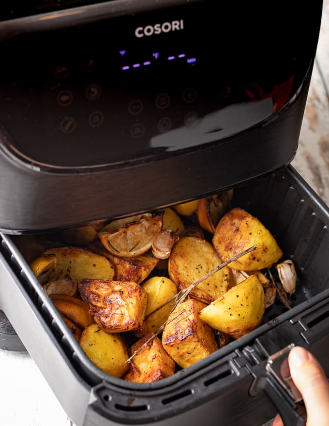 the basket of an air fryer being opened to show the potatoes inside