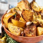 a terracotta colour bowl of roast potatoes with bits of lemon and garlic