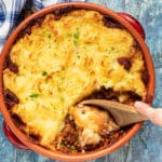 Lentil Shepherd's Pie in a terracotta dish with a wooden spoon digging in