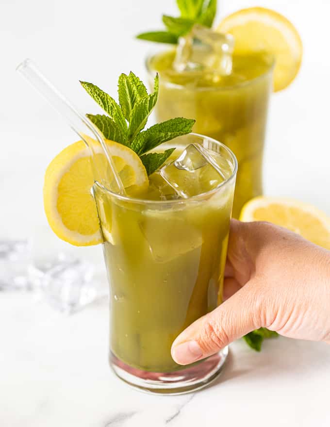 a hand picking up a glass of matcha lemonade 