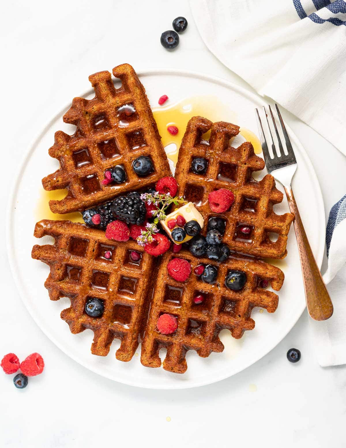 a white plate with oatmeal waffles, berries and maple syrup