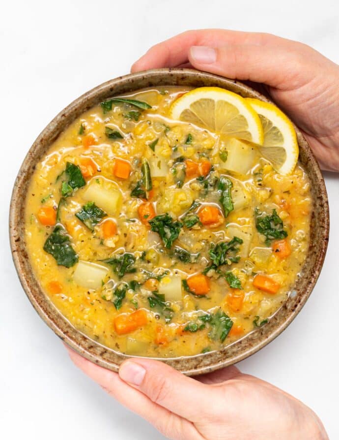 two hands holding a bowl of red lentil soup with lemon 