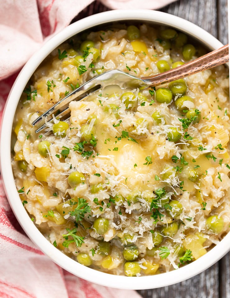 a bowl of Risi e Bisi (Italian Rice and Peas) in a bowl with a fork, topped with vegan butter and fresh parsley