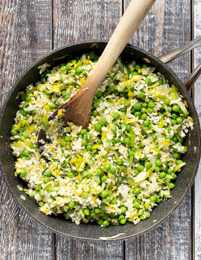 risotto rice, peas, onions and leeks cooking in a pan