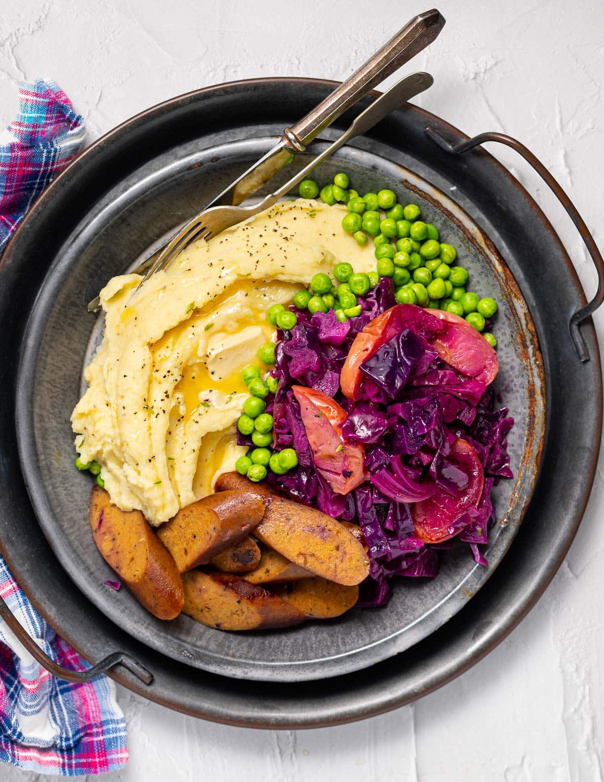 a plate of mashed potato, sausage, red cabbage and peas