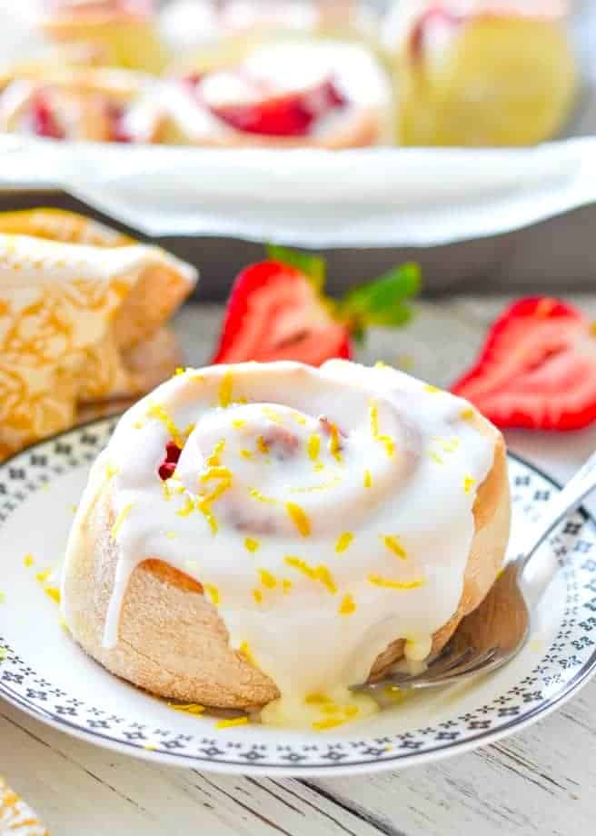 a lemon strawberry roll covered in frosting and lemon zest on a small plate 