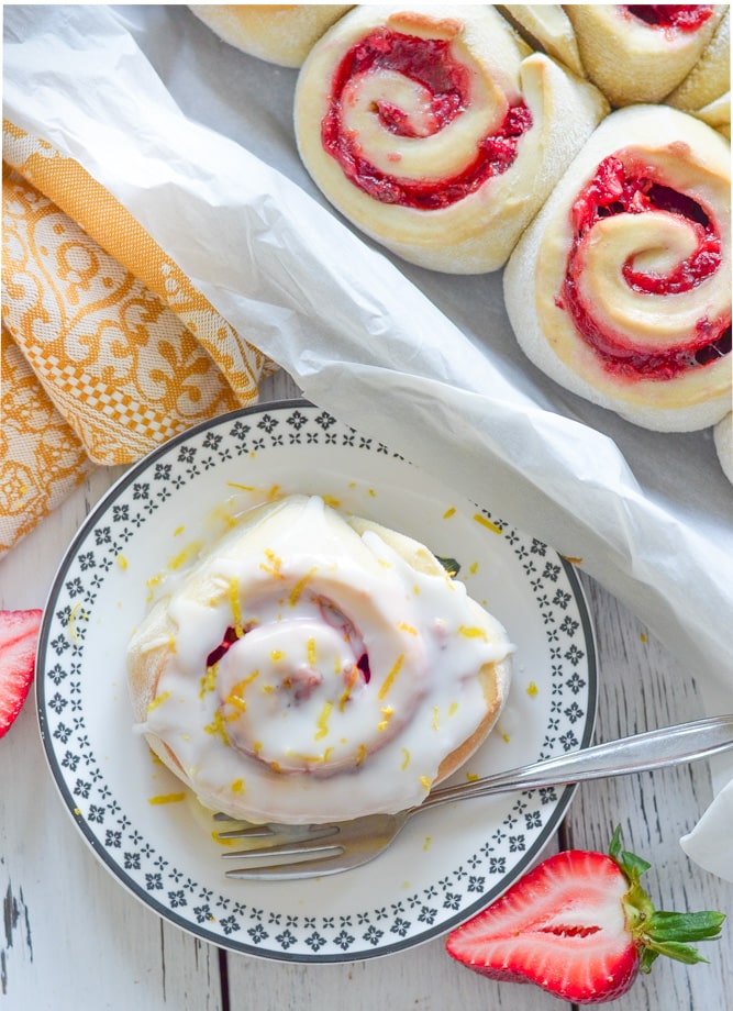 overhead shot of strawberry rolls. One frosted on a plate. Others unfrosted in tin.