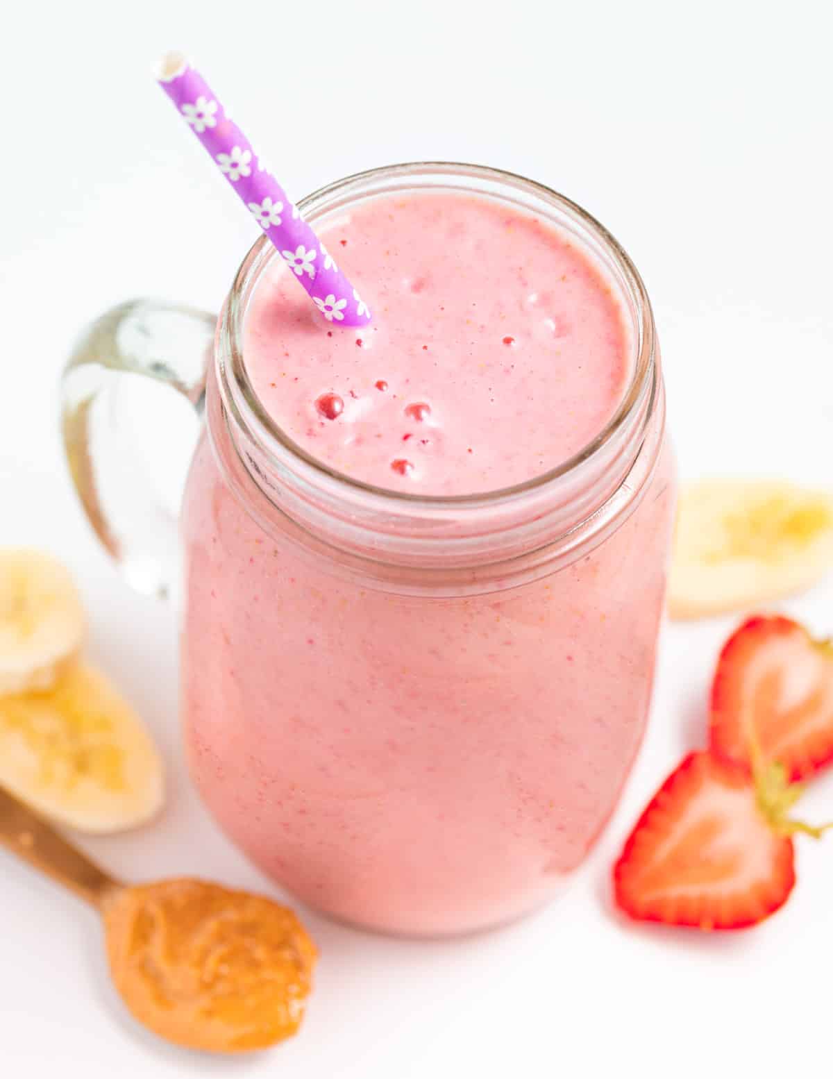 a strawberry banana peanut butter smoothie in a glass with a straw