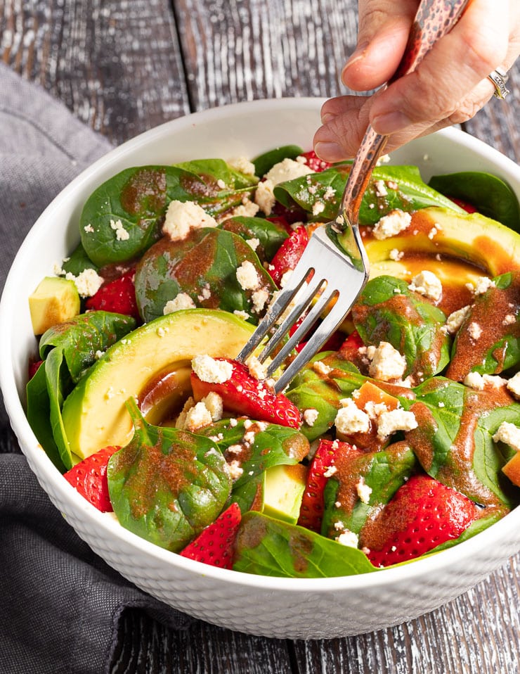 a fork digging in to a bowl of strawberry spinach salad 