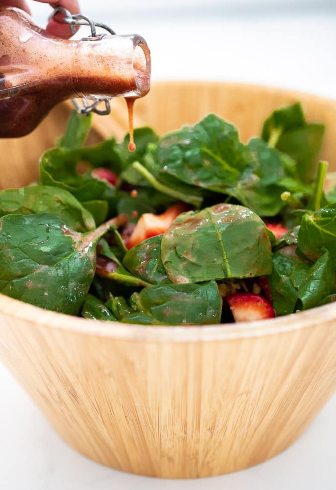 Strawberry vinaigrette being drizzled over leafy greens