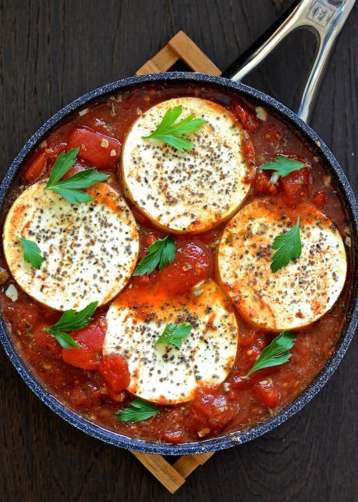 Vegan Shakshuka in a pan - tofu rounds in a spicy tomato sauce with cilantro leaves sprinkled over 