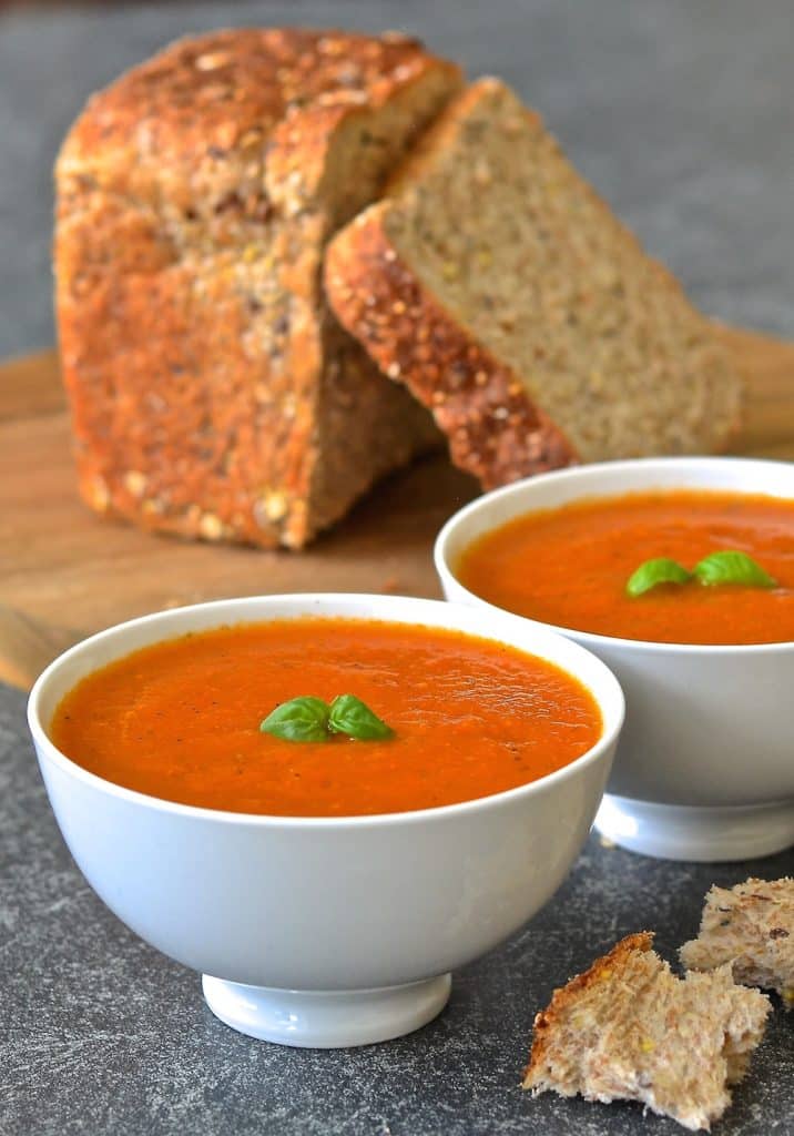 Easy Tomato Basil Soup in bowls, topped with fresh basil. A loaf of cut bread in background. 