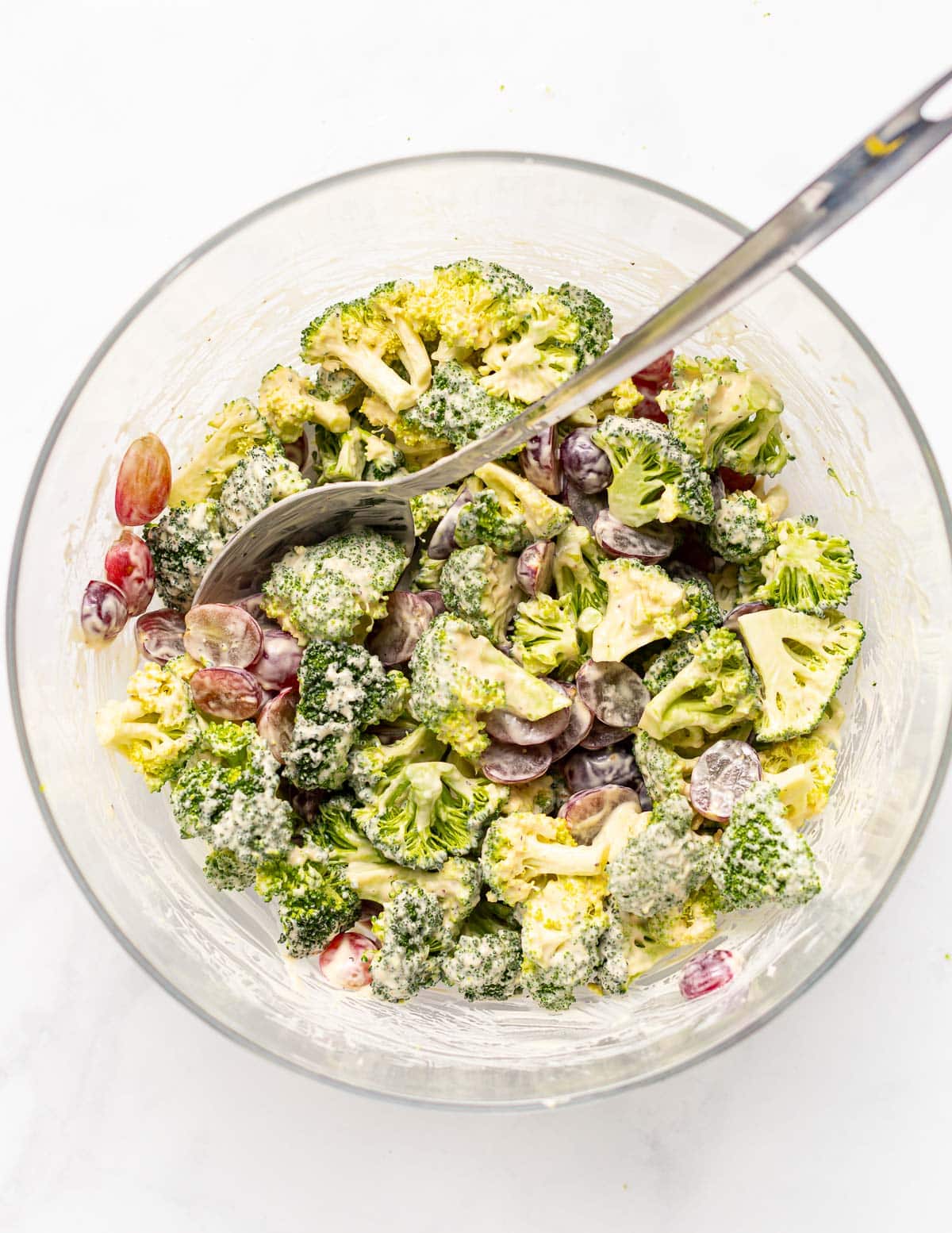 a bowl of vegan broccoli salad with a spoon in it