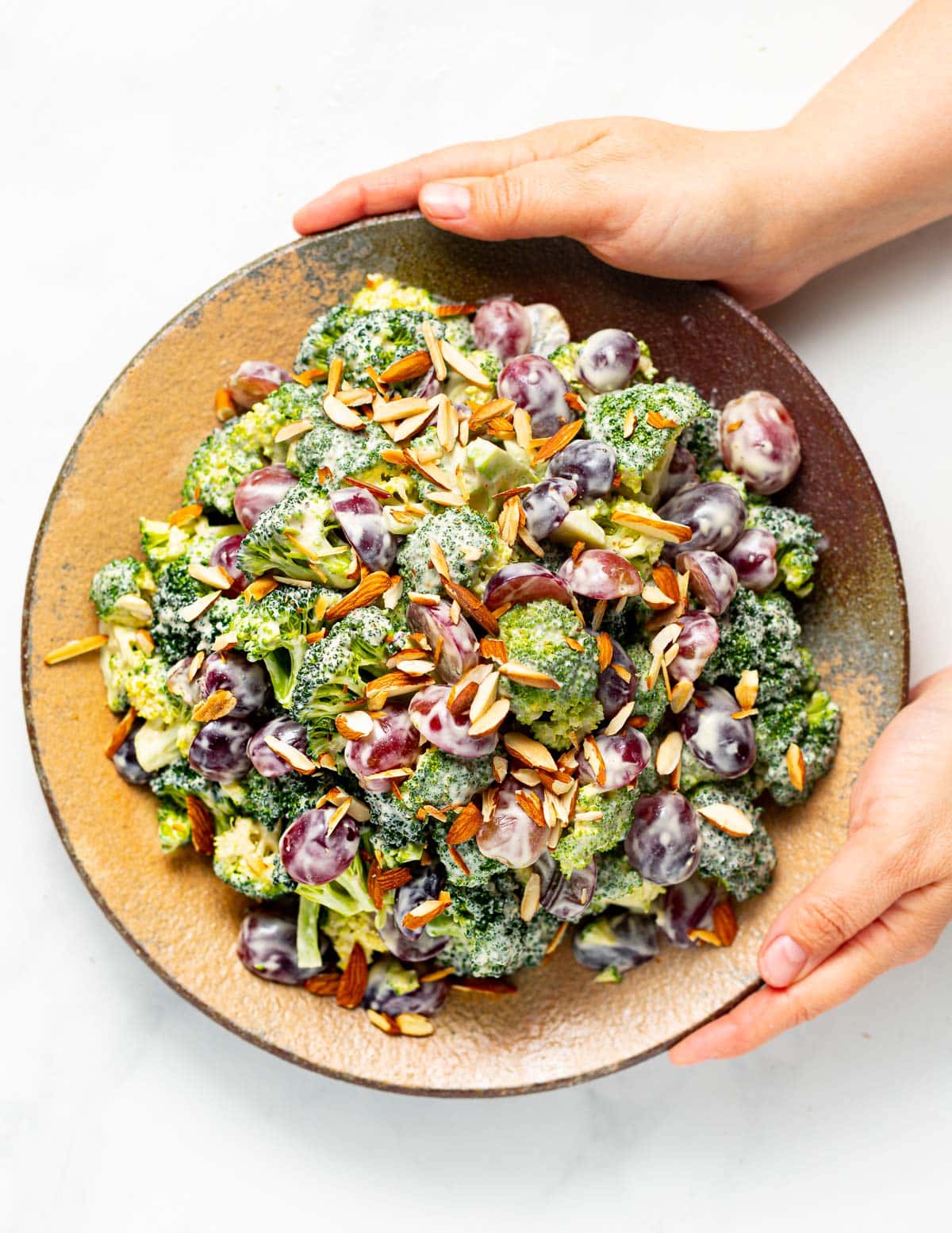 hands holding a rustic plate filled with vegan broccoli salad 
