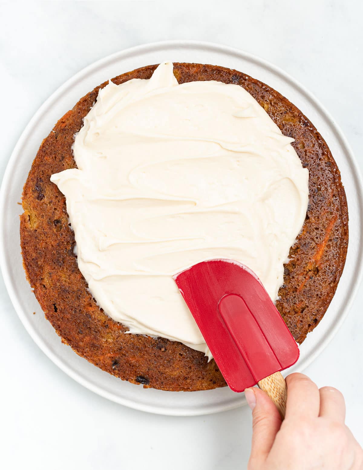 vegan cream cheese being spread on a cake layer with a red spatula