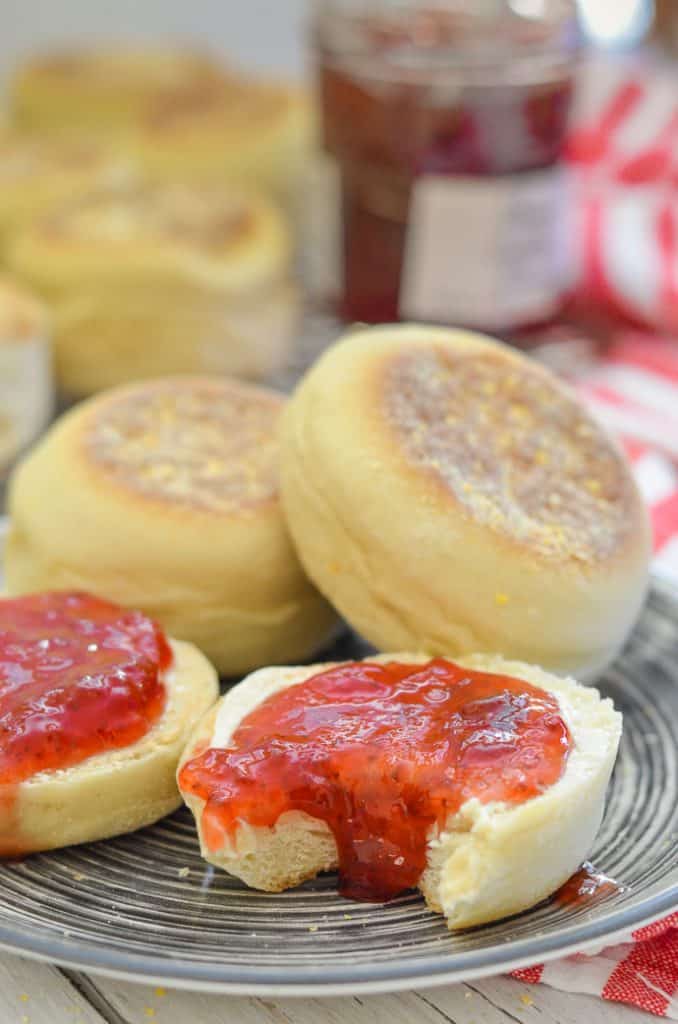 Close up Shot of Homemade English Muffins on a plate. Split, spread with drippy jam with a bite taken out.