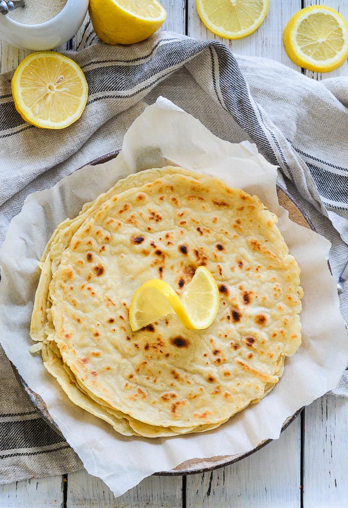 Vegan English Pancakes piled on a plate with a twirl of lemon