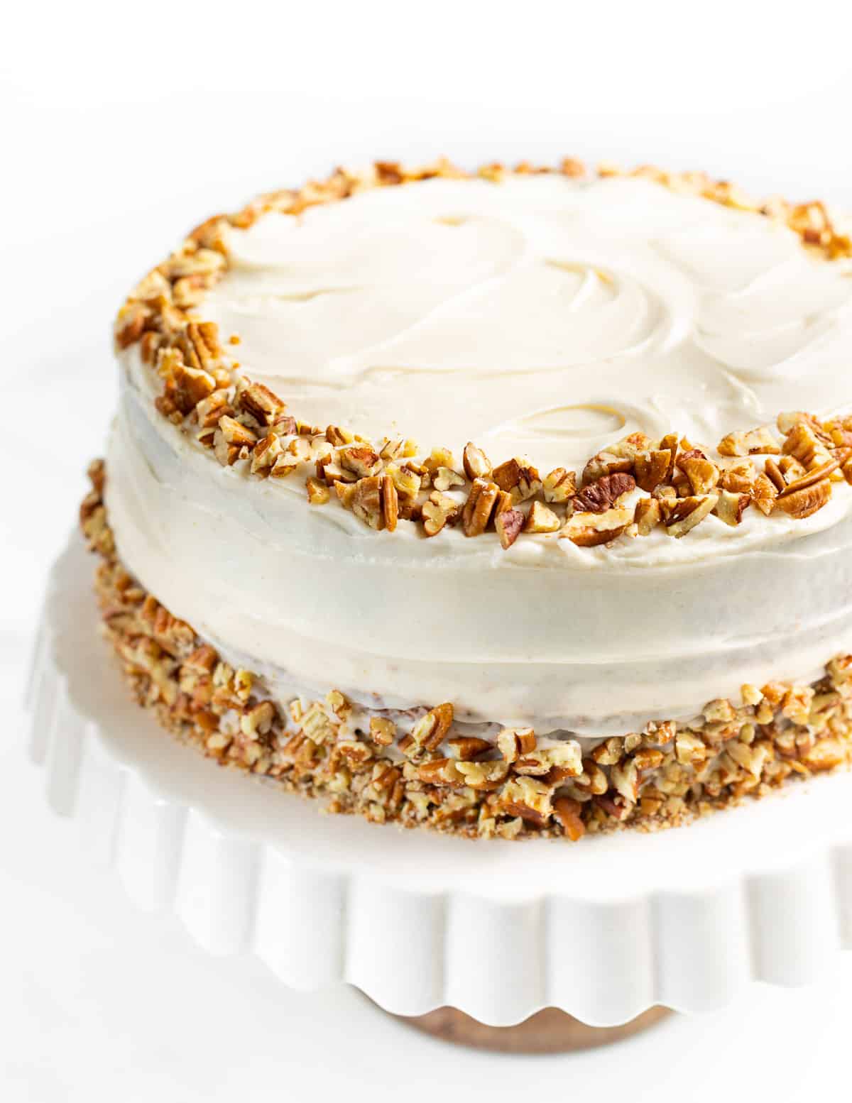 a large vegan hummingbird cake decorated with cream cheese frosting and pecans