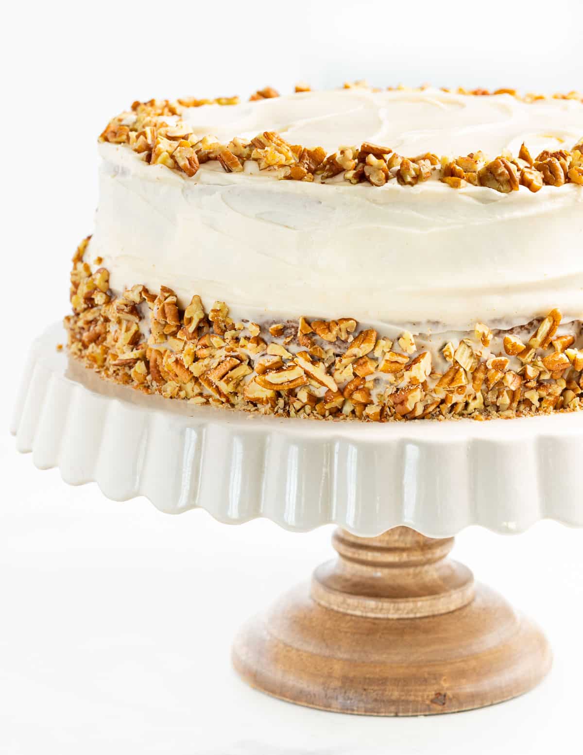 a vegan hummingbird cake decorated with cream cheese frosting and chopped pecans