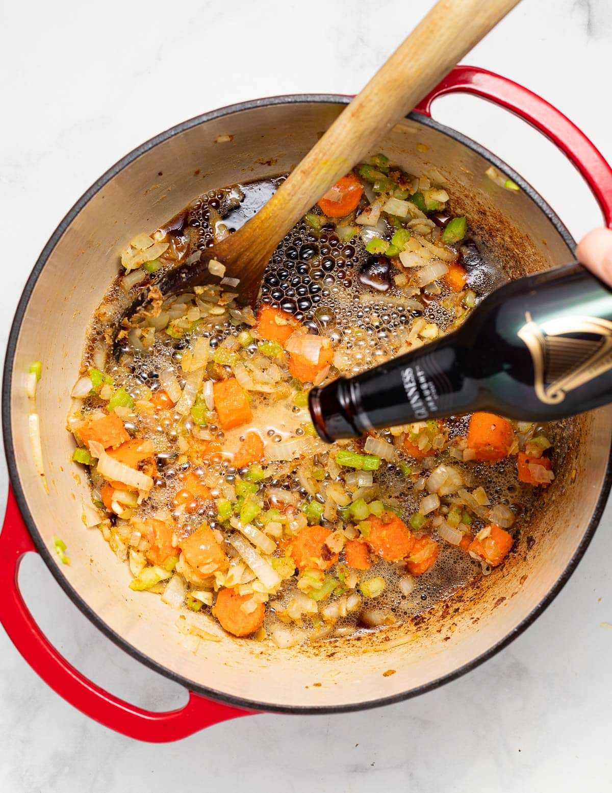 Guinness being poured in a pan with some vegetables