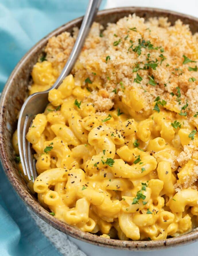 a close up photo of a bowl of vegan mac and cheese with a fork on the side