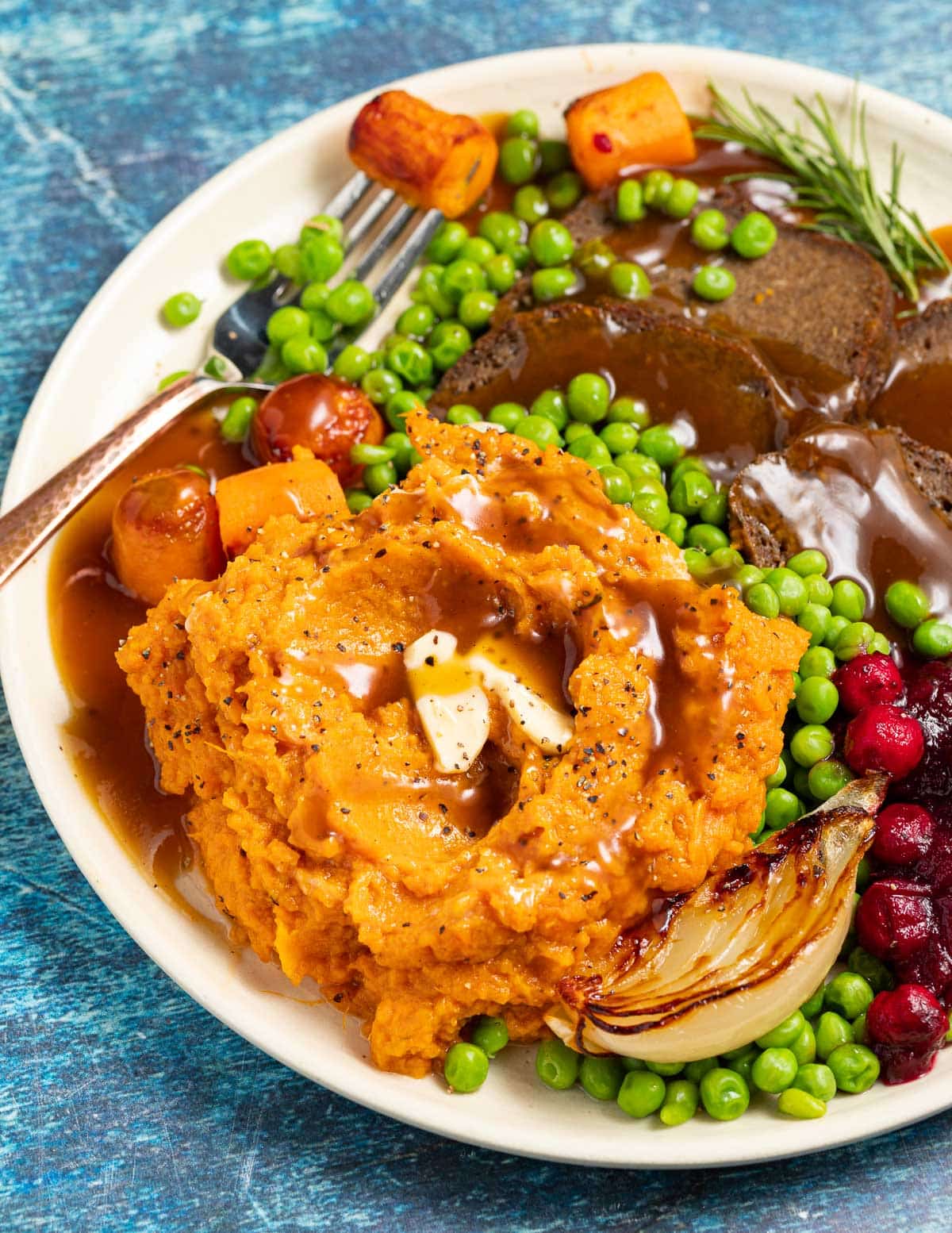 mashed sweet potatoes, peas, cranberry sauce and sliced vegan seitan on a plate with lots of gravy