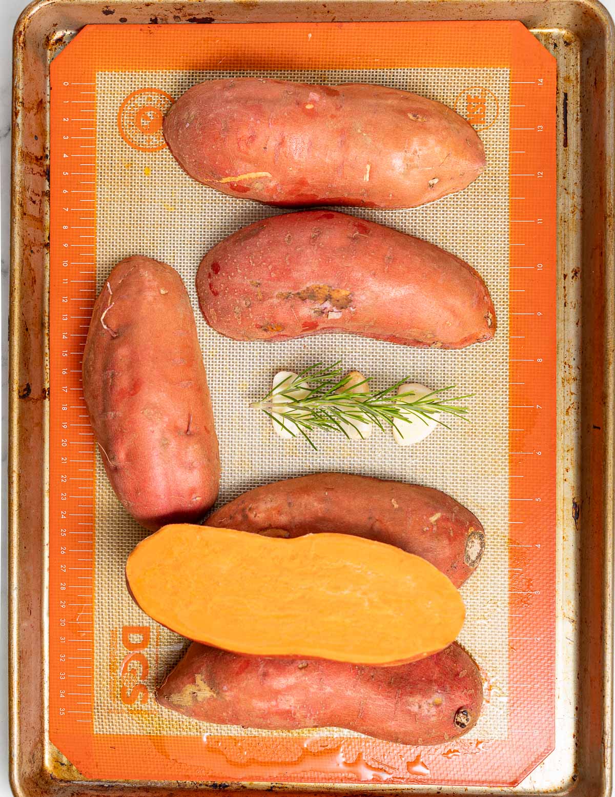 halfed sweet potatoe son a tray with rosemary and garlic