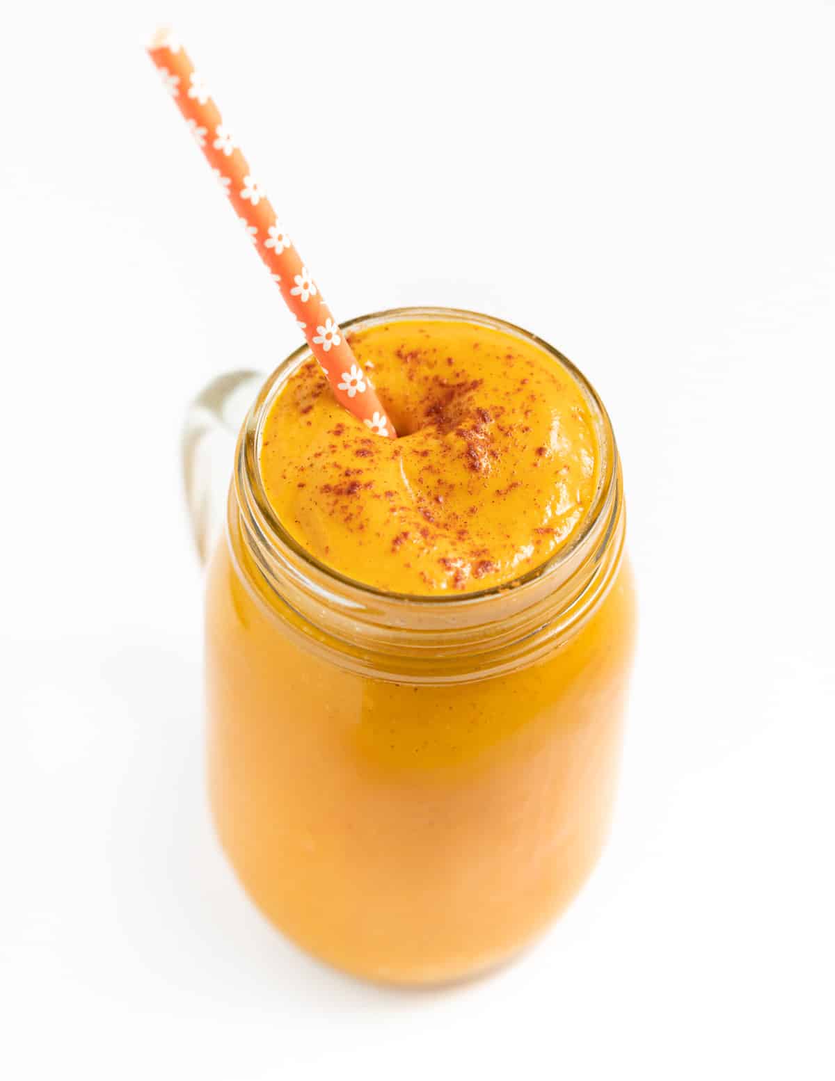 a glass of vegan pumpkin smoothie with an orange flowery straw