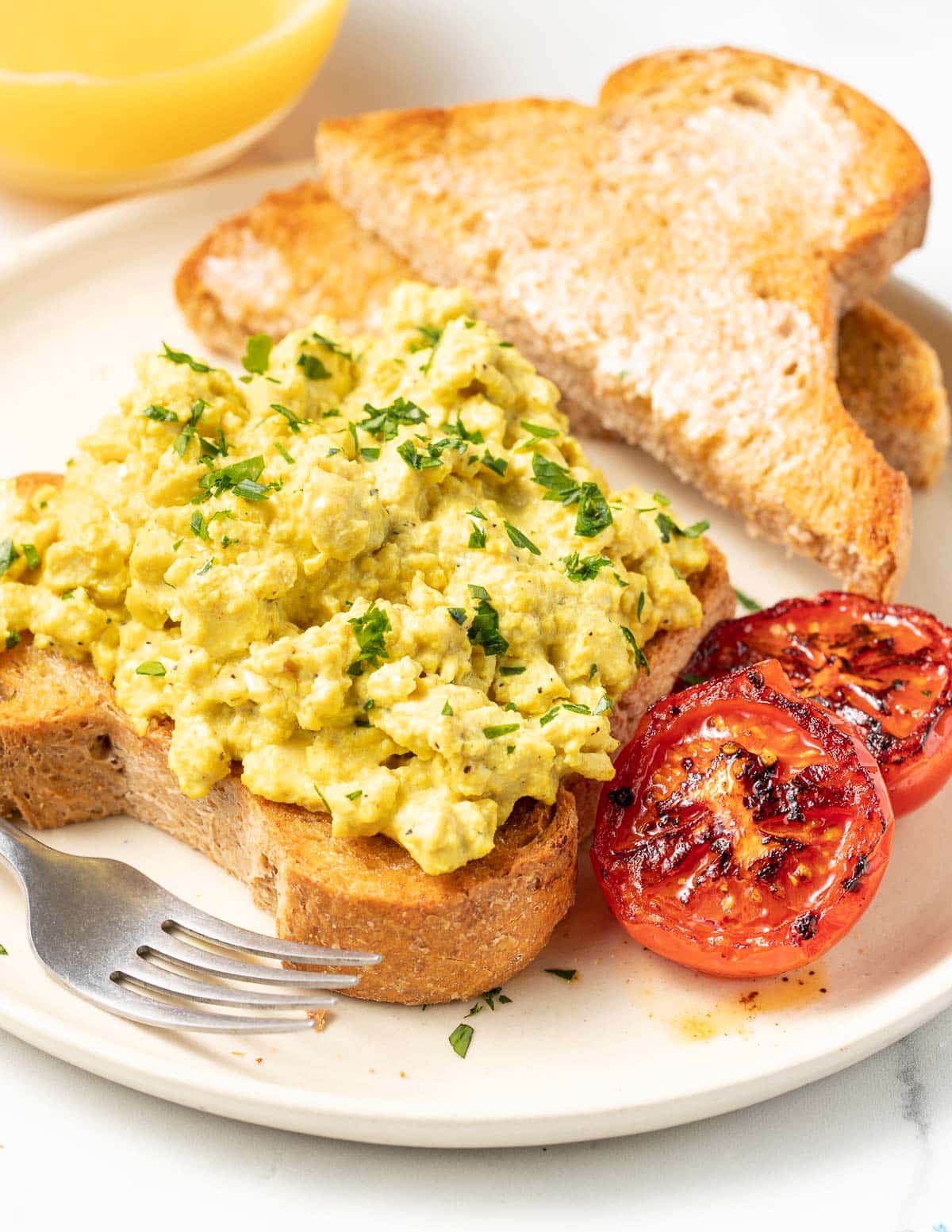 a place of vegan scrambled eggs with tomatoes and a glass of orange juice
