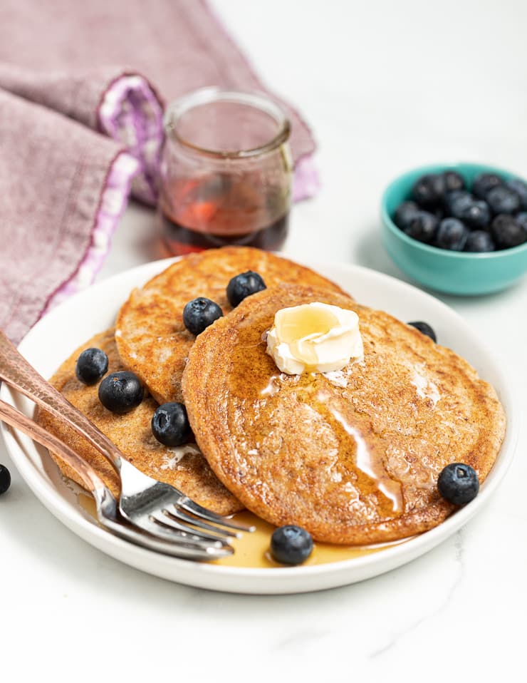  a plate of vegan spelt pancakes with vegan butter, blueberries and maple syrup