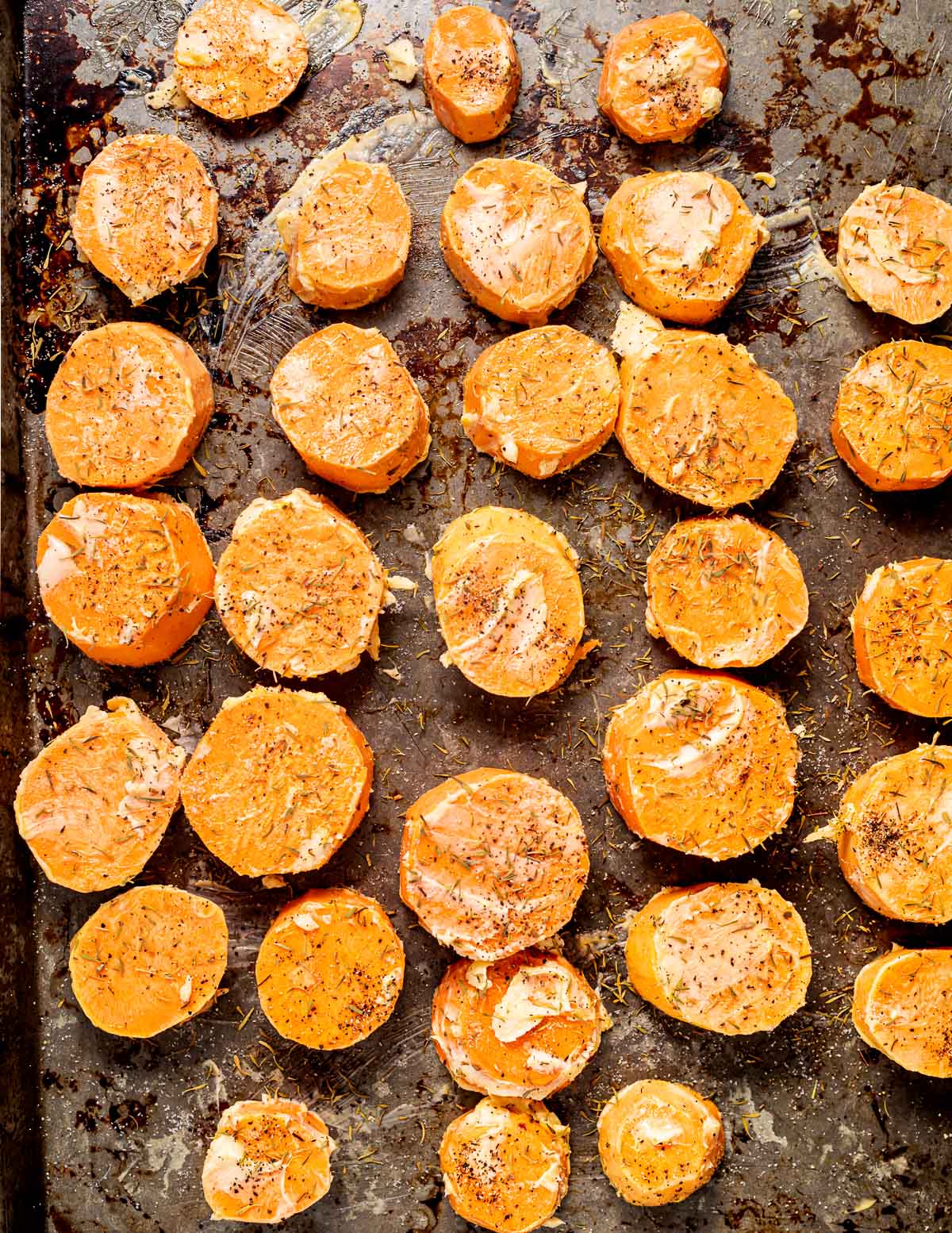 a tray of raw sweet potato rounds coated in vegan butter, herbs and seasoning