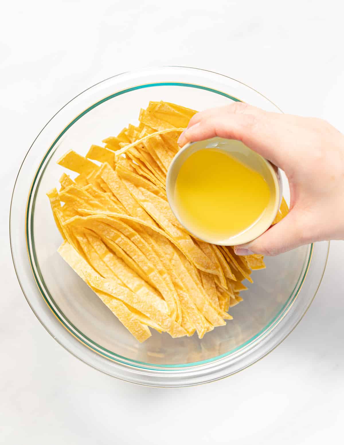oil being poured over tortilla strips in a bowl
