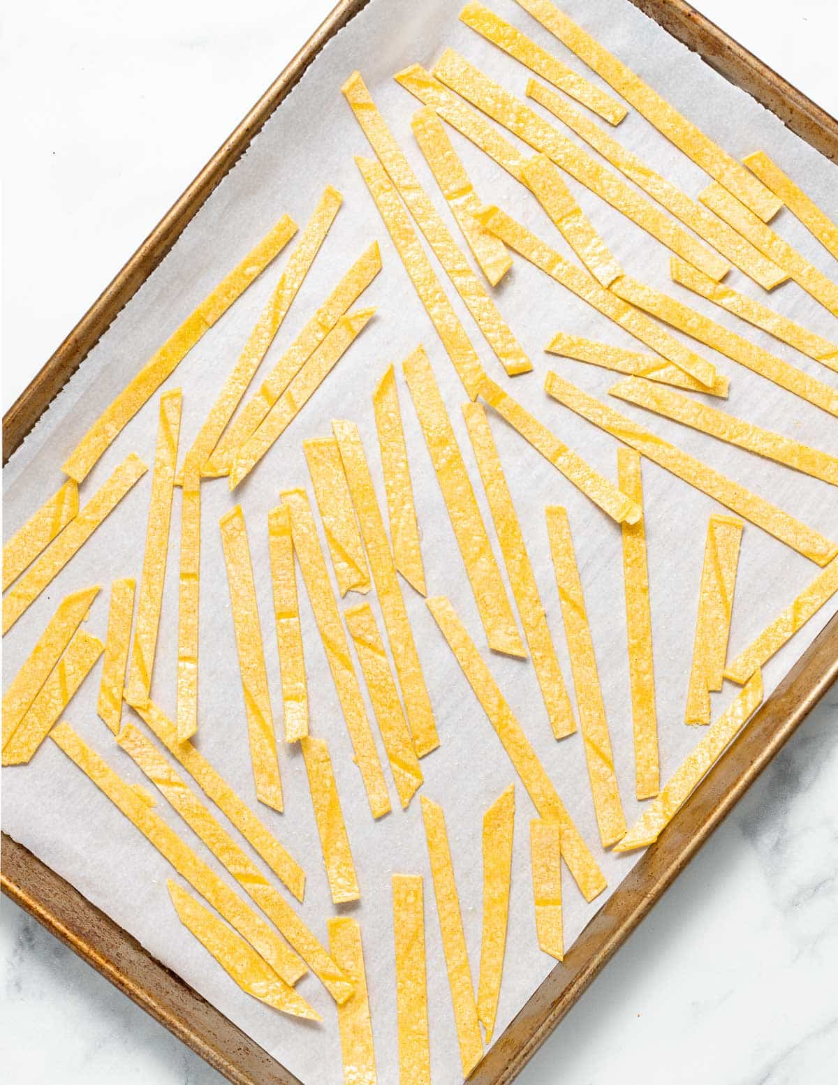 uncooked tortilla strips laid out on a baking parchment lined tray