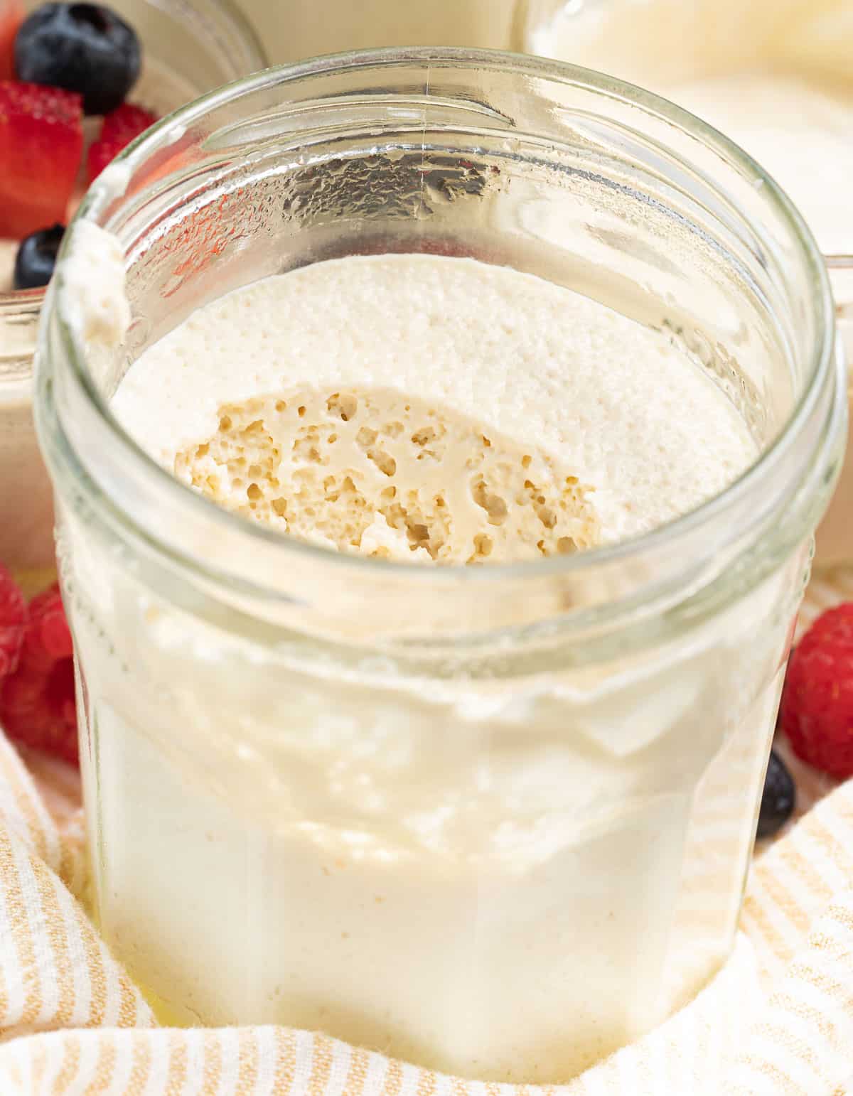 thick vegan yogurt in a jar with a spoon removed showing the bubbly fermented texture