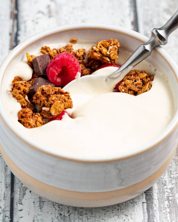a bowl of vegan yogurt topped with granola and fresh raspberries